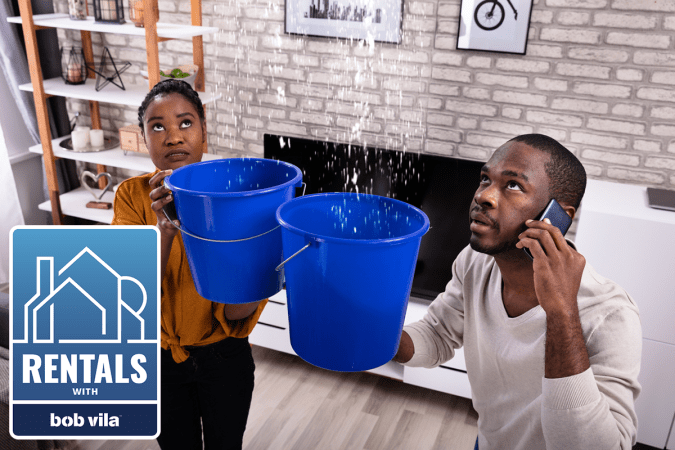 couple holding buckets to catch water leaking from rental property ceiling