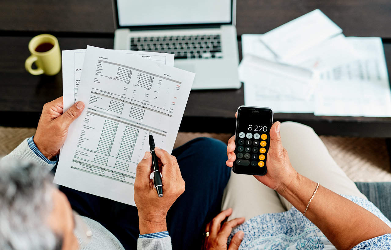 overhead shot of people looking at financial documents and one is holding an iphone calculator