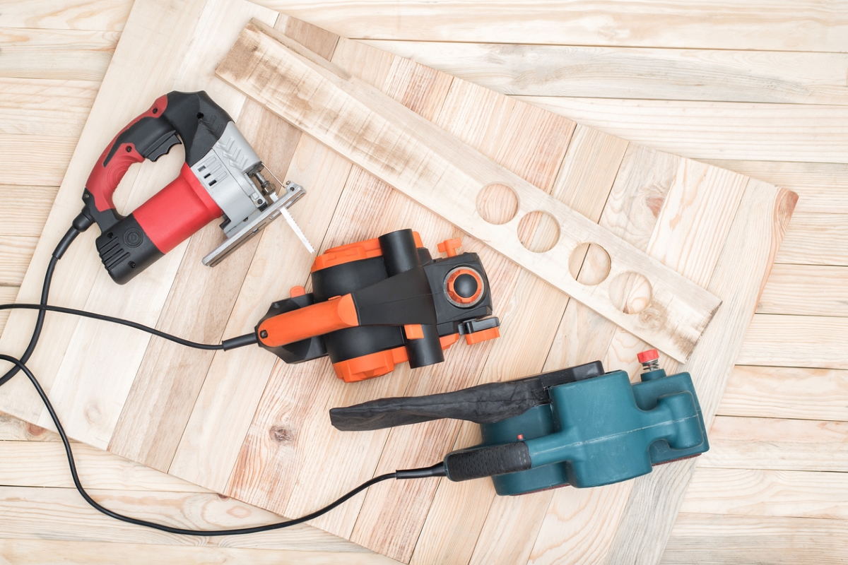 Three power tools laying on sheets of plywood.