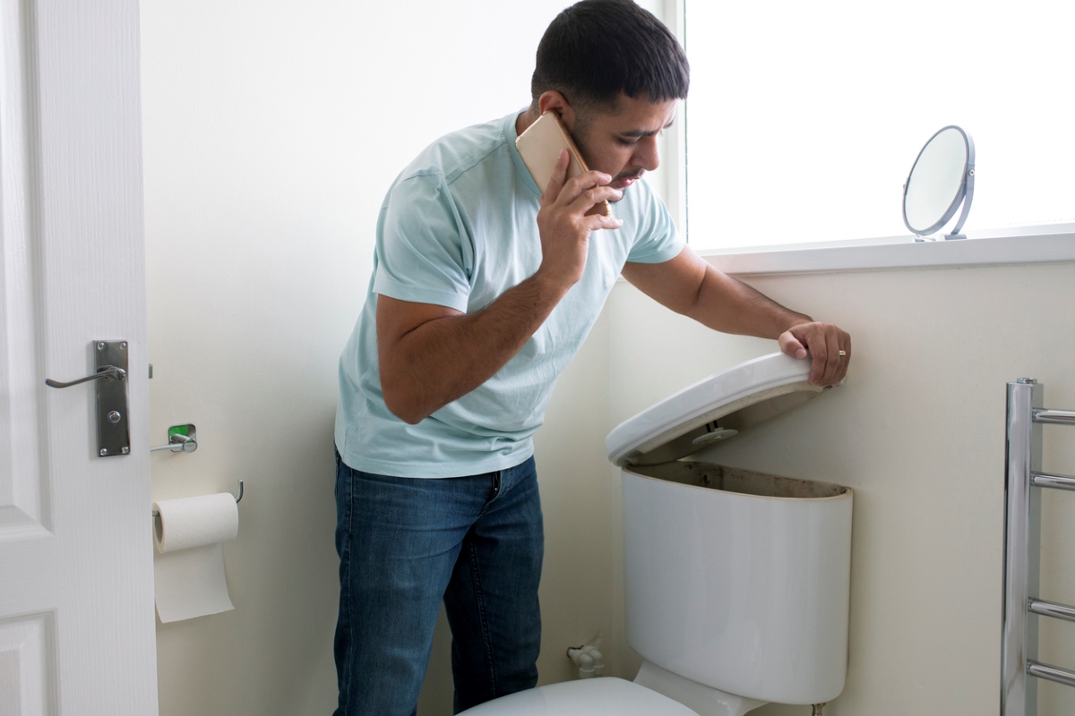 Man on phone opening toilet tank