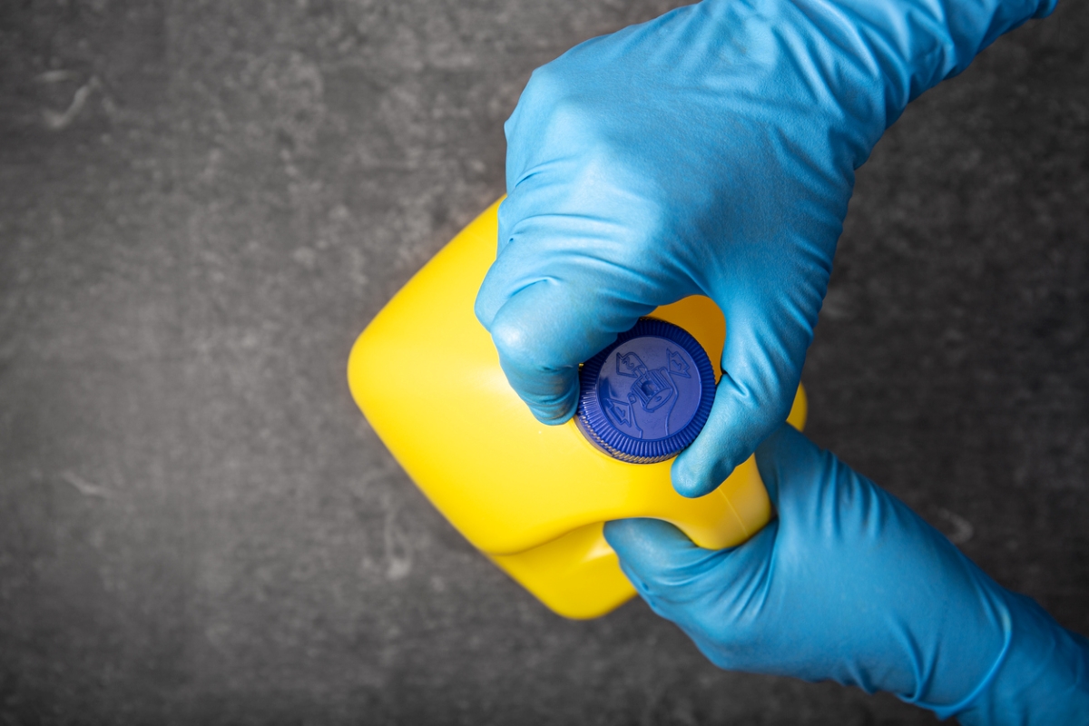 Blue gloved hands opening yellow bottle of bleach