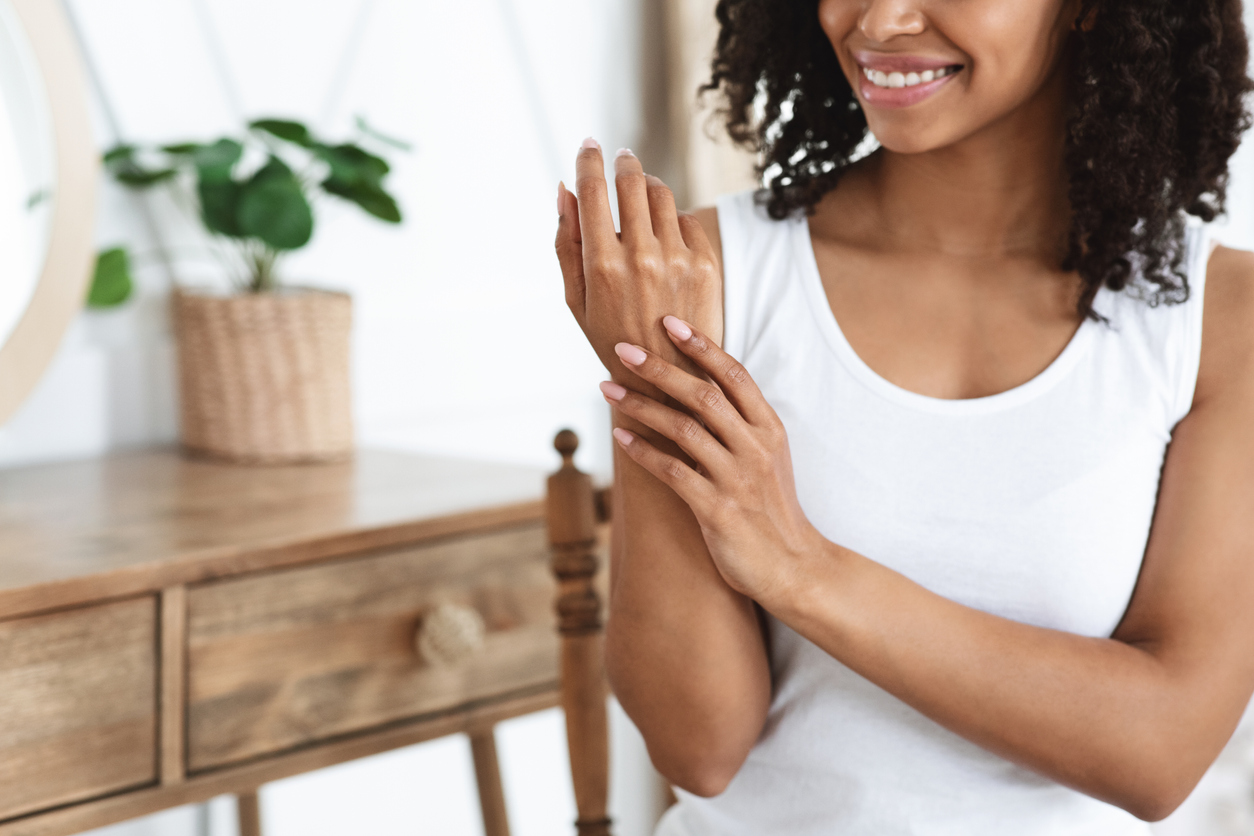 smiling woman applying hand lotion to arms and hands