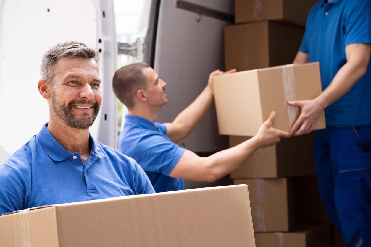 professional movers in blue polo shirts holding boxes and loading them onto a truck