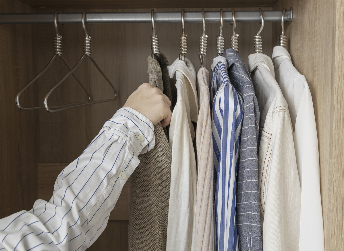 a hand reaches for a jacket in a closet full of metallic hangers and shirts