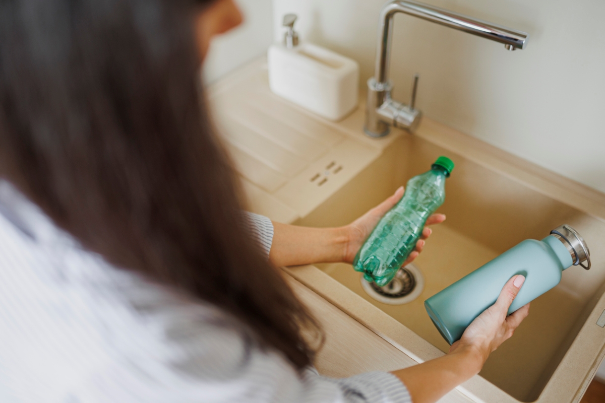 Woman holding plastic bottle in one hand and reusable bottle in other