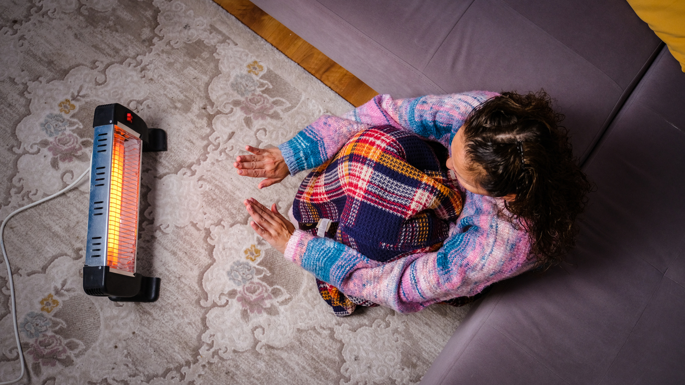 Person sitting on the floor heating their hands at home over a portable electric halogen heater