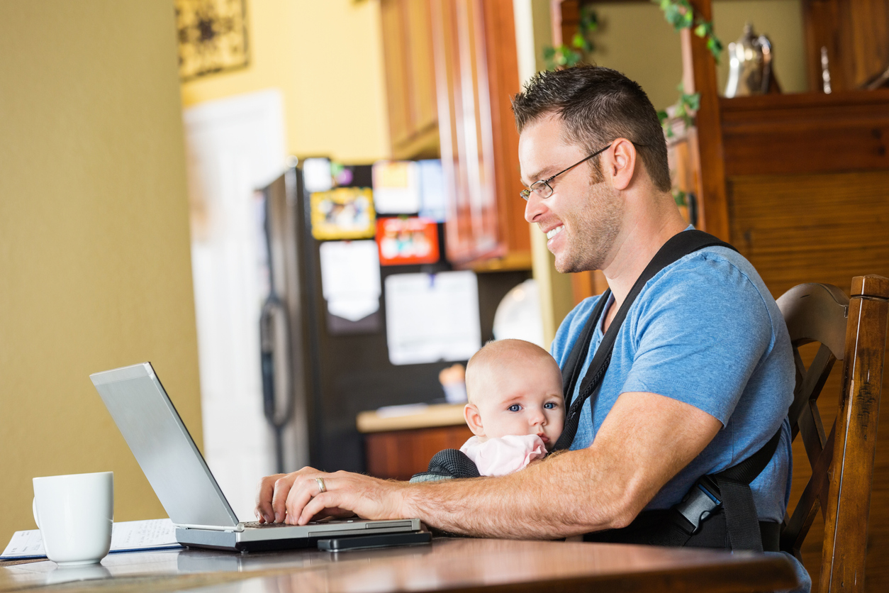 father smiling while taking care of baby and working