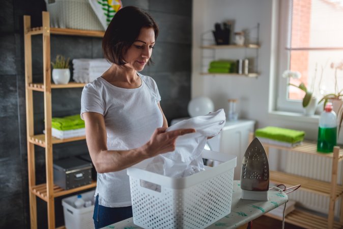 woman in laundry room holding piece of white laundry just cleaned