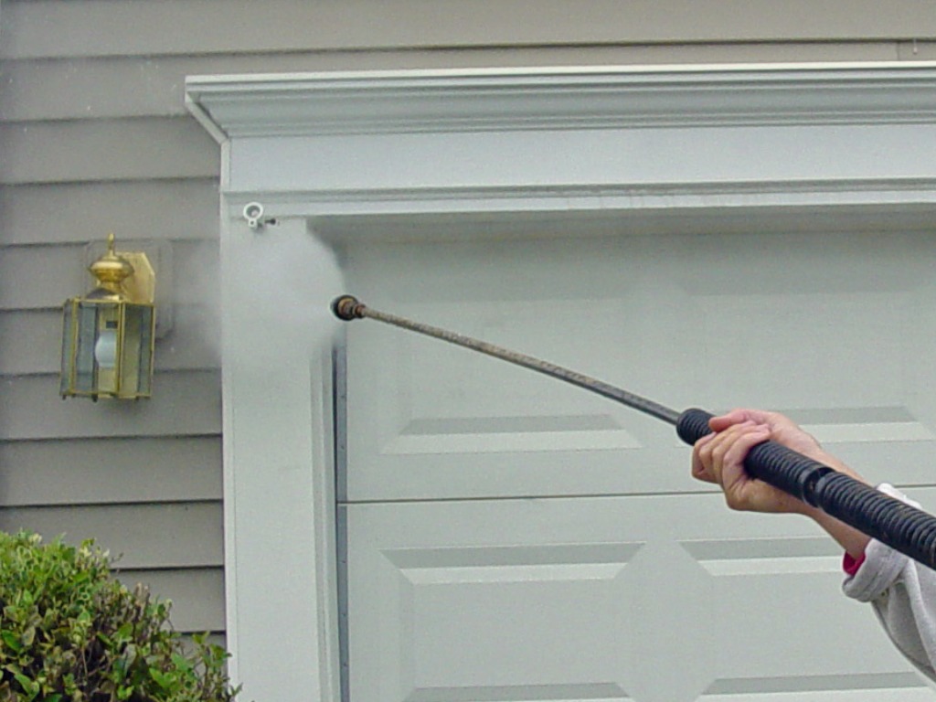 woman power washing garage with light figure on left side of garagejpg