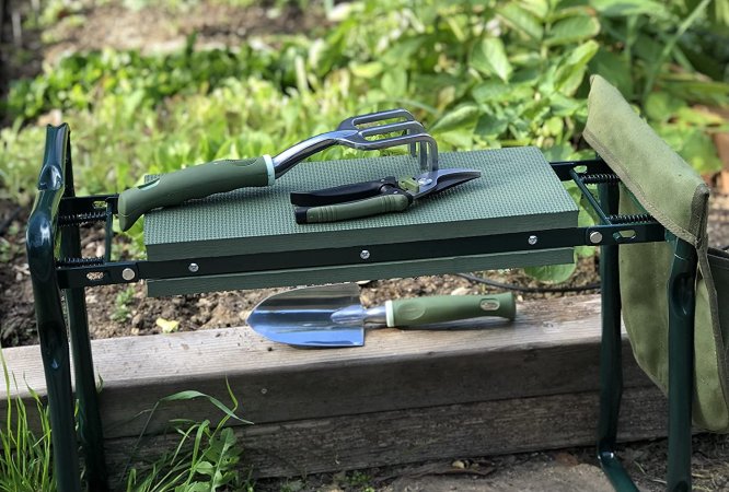 The best garden kneelers option pictured next to a garden plot with gardening tools