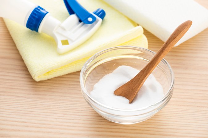 Citric acid powder in a small glass bowl next to a spray bottle, cloth, and sponge