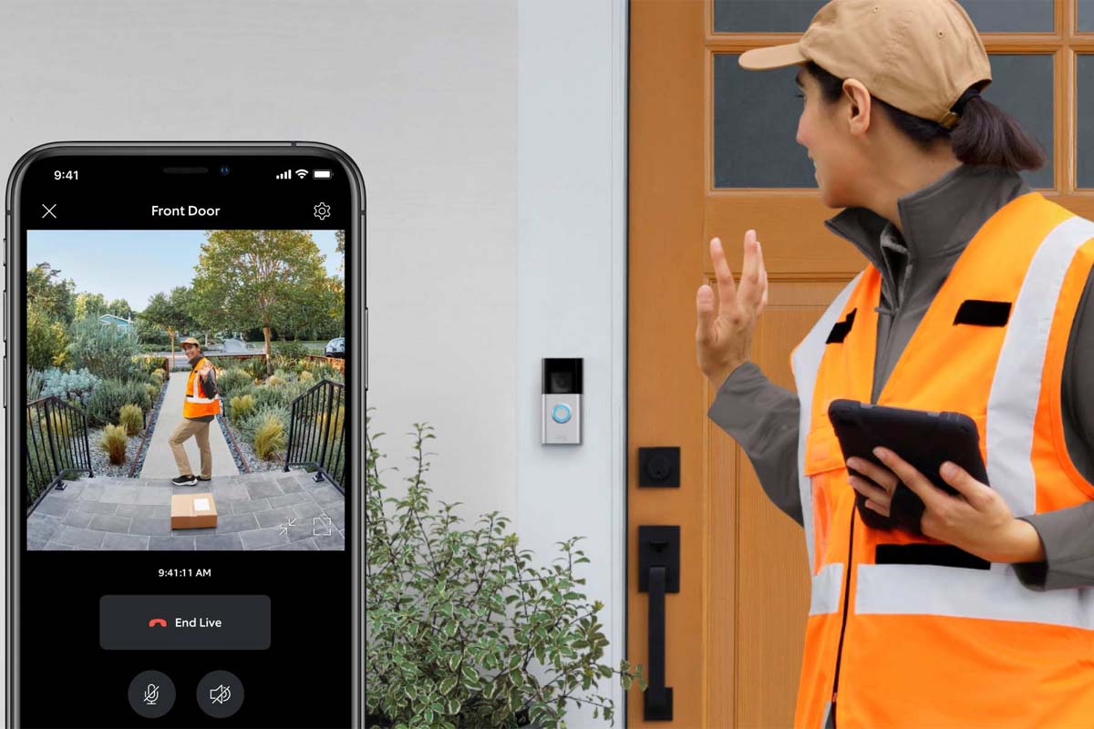 A delivery worker waves to a video doorbell installed by a front door while the homeowner views the footage on their phone app.