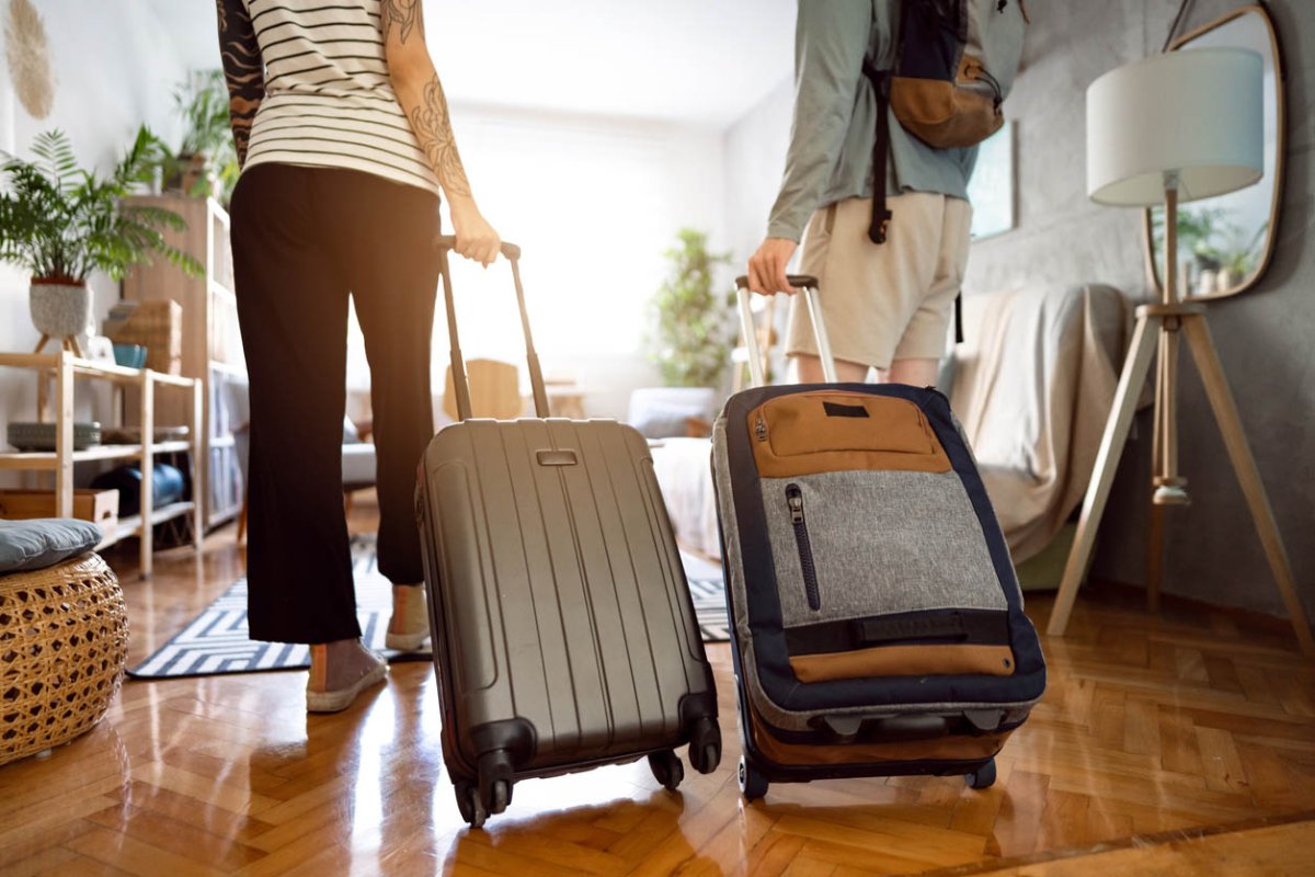 Two people leaving a room in a home while dragging suitcases.