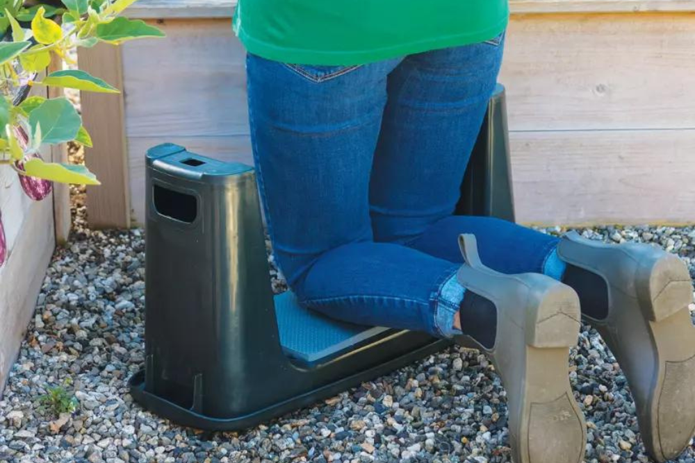 A gardener kneeing on the best garden kneeler option placed on gravel