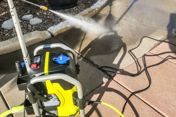 A person using the Ryobi pressure washer 2000 PSI to clean a concrete patio