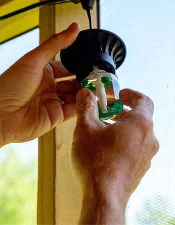 A close-up of a person screwing a bug repellent diffuser into the Tiki BiteFighter LED String Lights