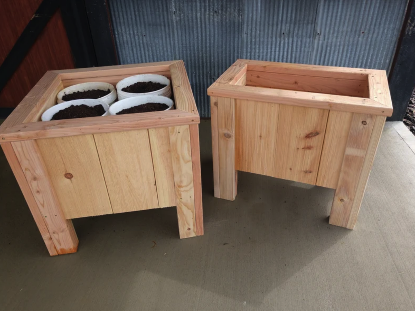 two square wooden planter boxes on legs on with white buckets full of soil inside