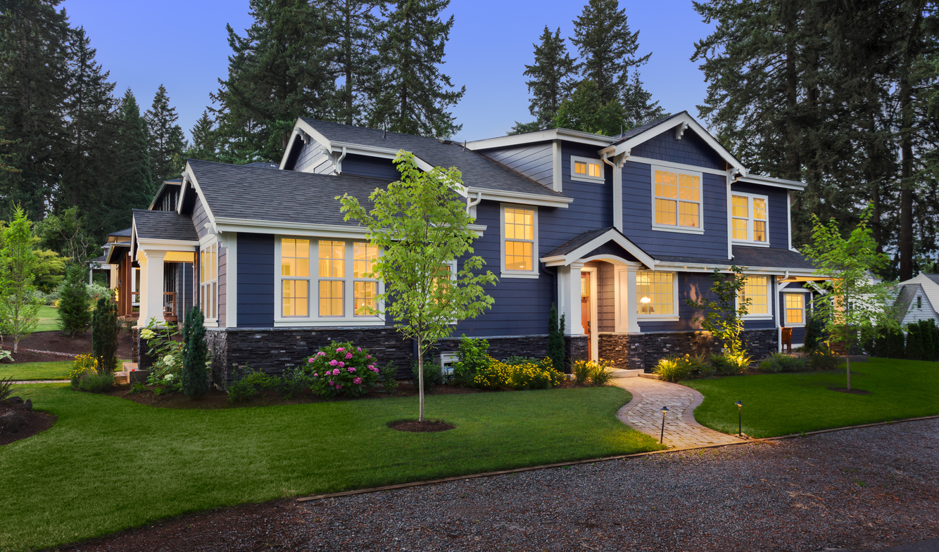 beautiful dark blue colored house surrounded by trees with lights on in windows in the evening