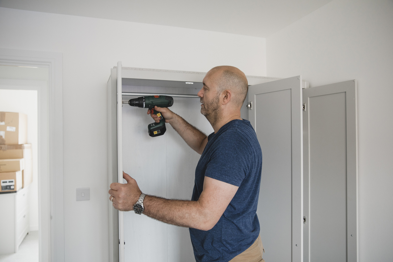 Mature man is building a wardrobe in the bedroom of his new home.