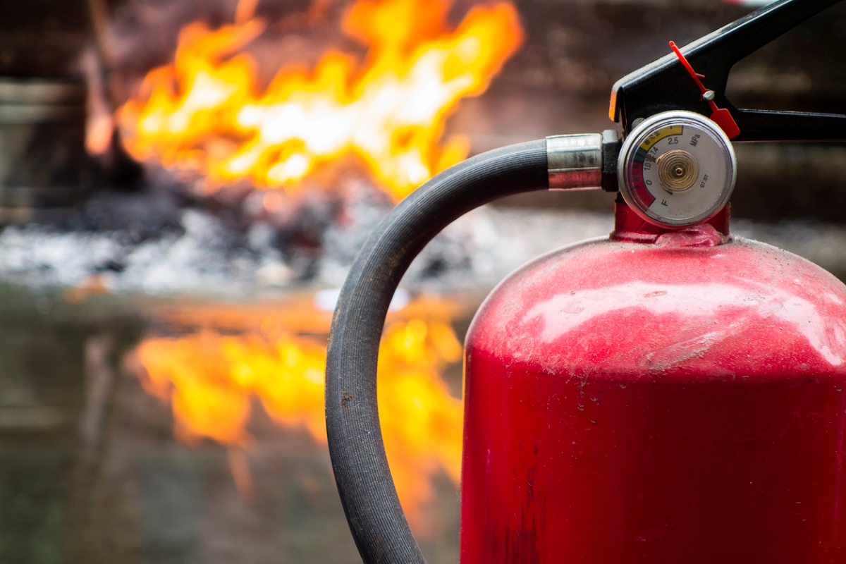 A fire extinguisher is in front of a fire in background burning in the background and reflecting on the ground.