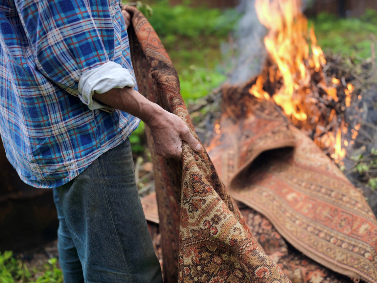 A person is throwing a tapestry rug into a burning pile of branches.