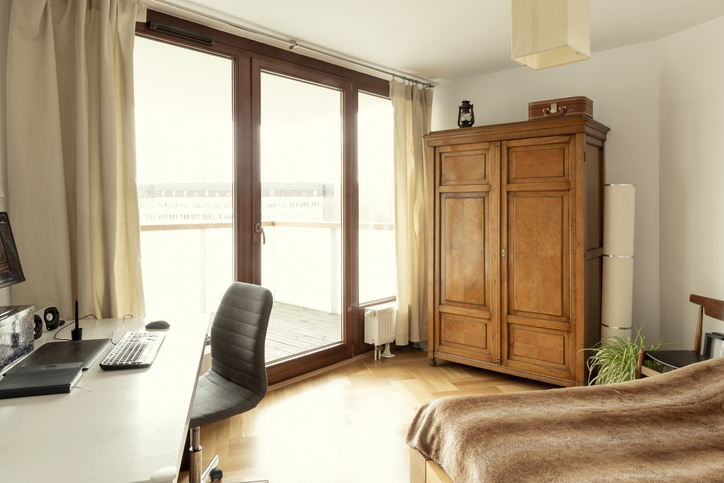 a-modern-apartment-with-desk-and-bed-and-wooden-armoire-along-with-floor-to-ceiling-windows-to-a-balcony