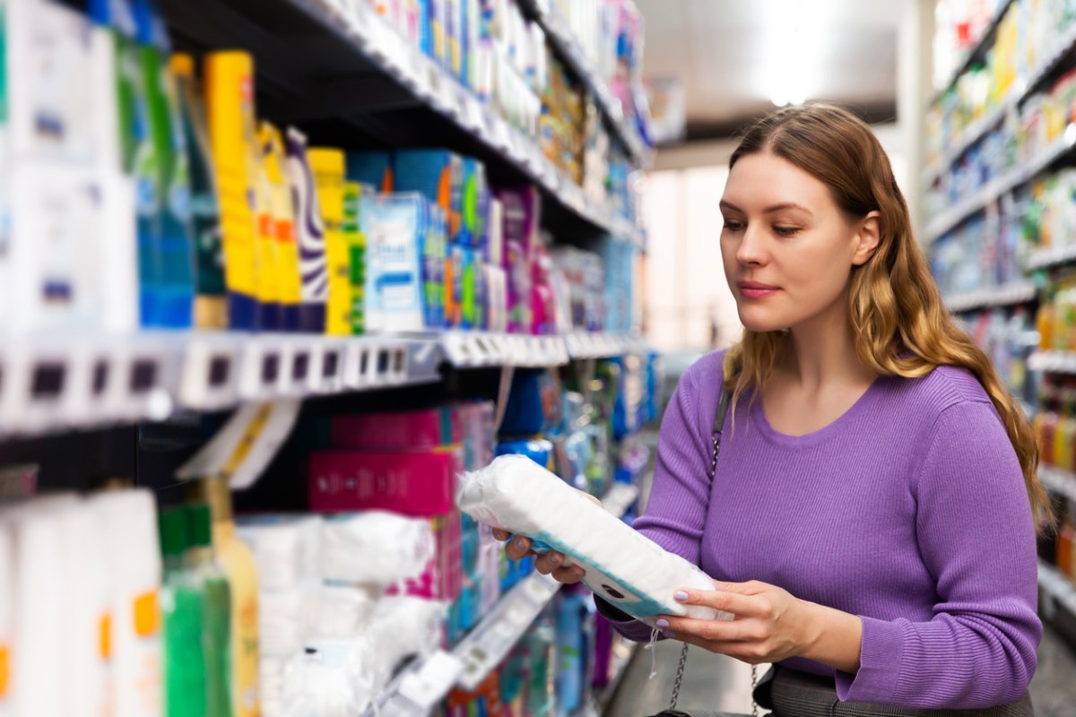 woman in purple sweater standing next to store shelf in aisle holding an item to purchase