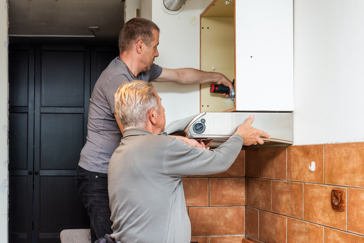 man helping older man remove kitchen vent hood and cabinet for responsible disposal during a sustainable kitchen remodel