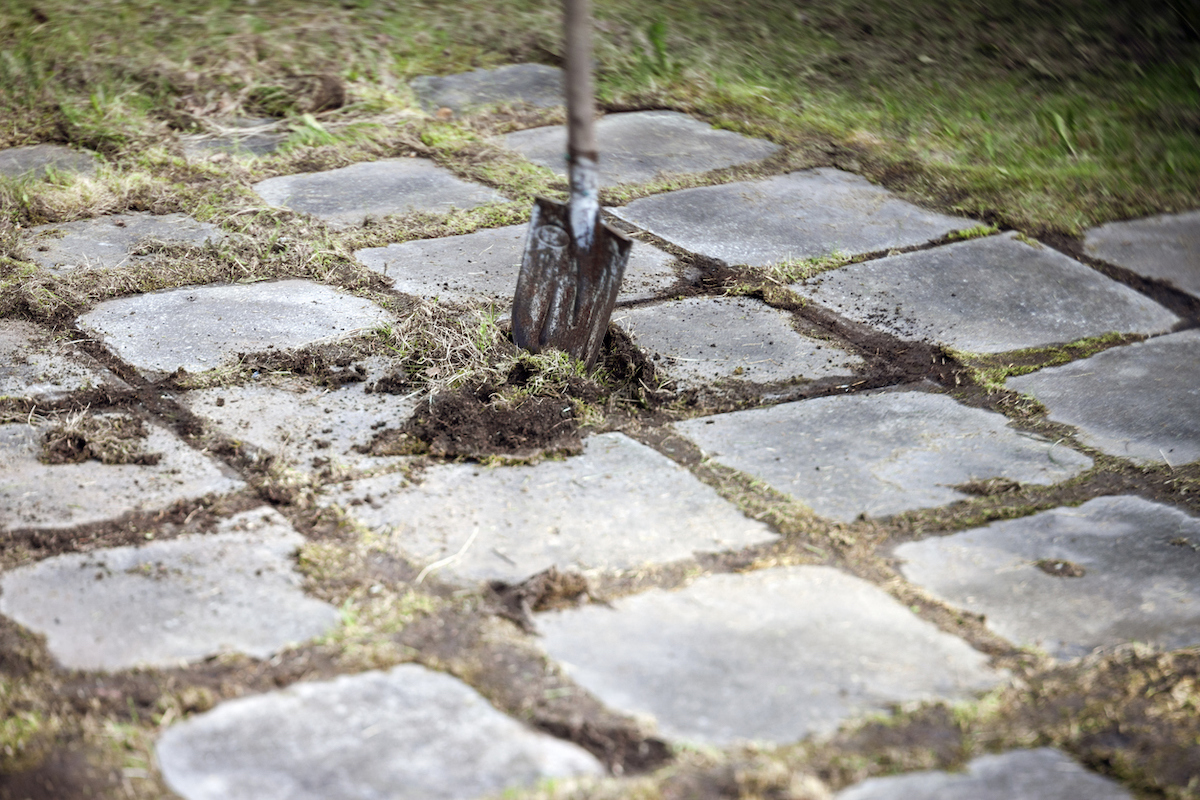 shovel digging up old concrete landscaping pavers to recycle or donate