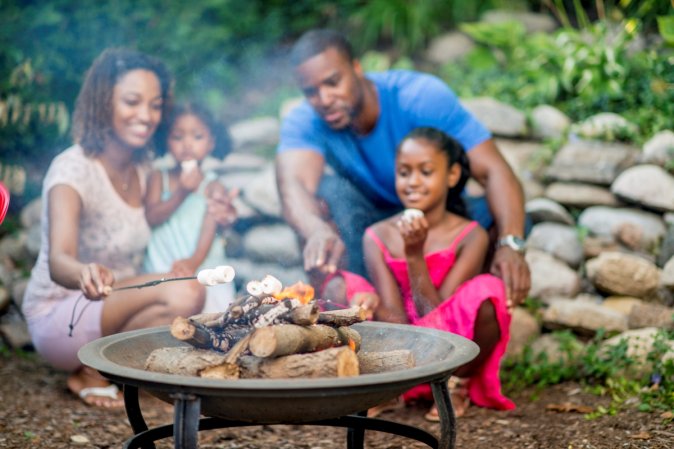 A family of four is roasting marshmallows in a fire pit in the outdoors.