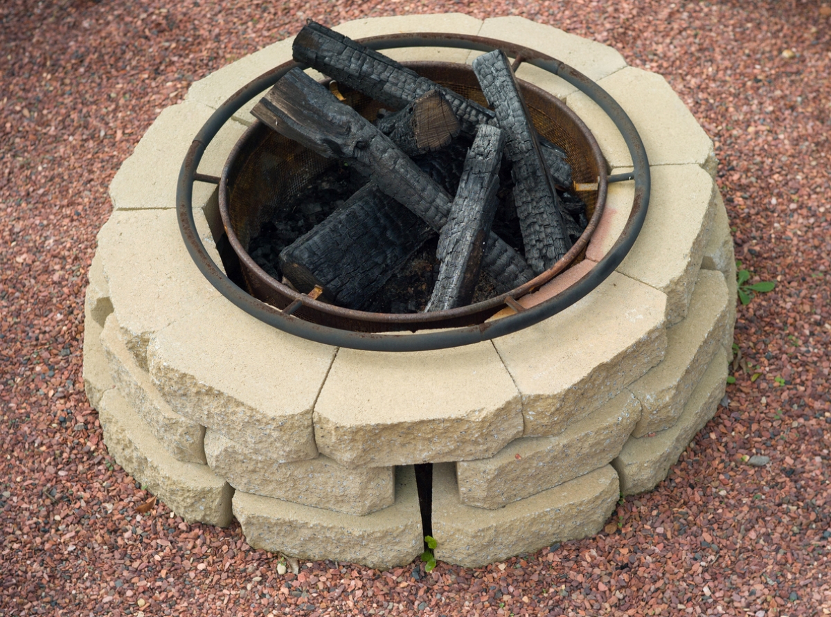 A circular light-colored stone fire pit contains burned logs.