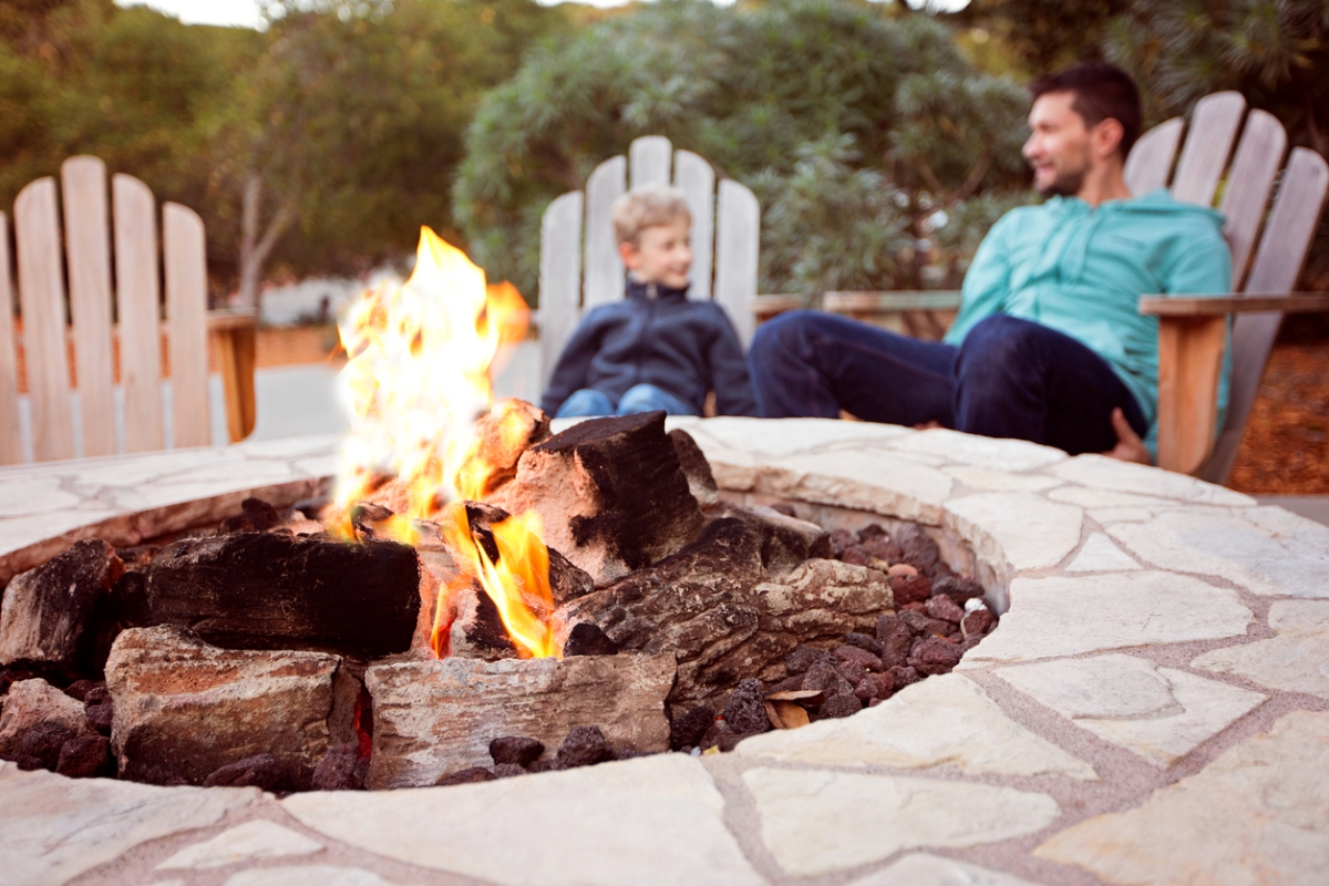 A father and son are sitting in Adirondack chairs behind a fire pit.