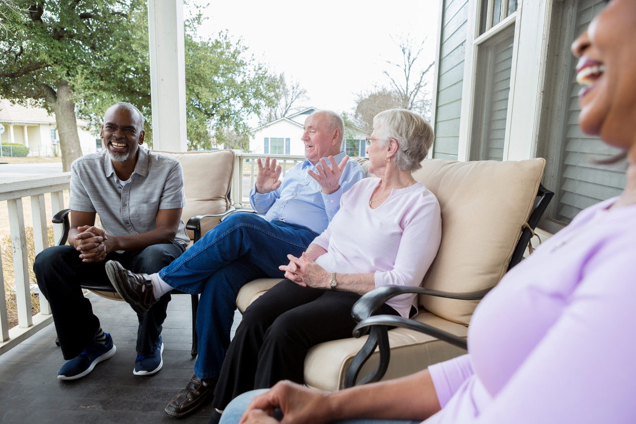 Active retired seniors enjoy one another's company while sitting on a porch together.