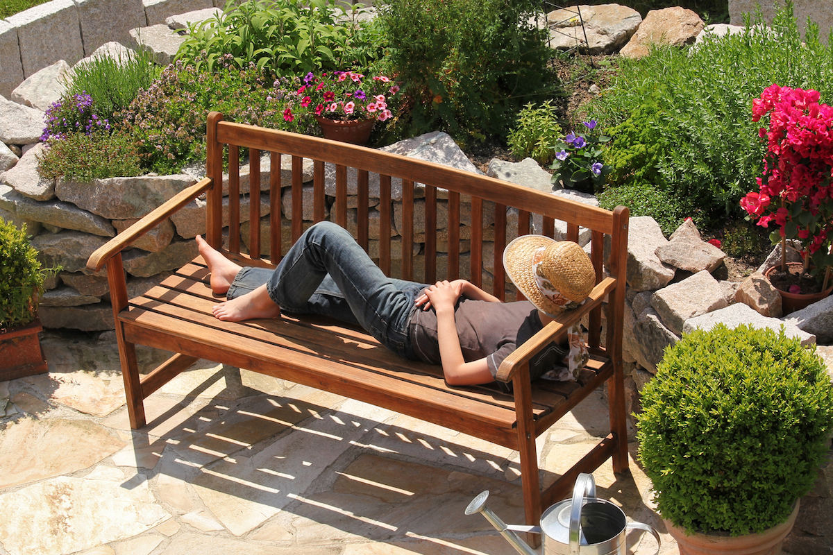 Woman laying on a wood garden bench surrounded by manicured landscape