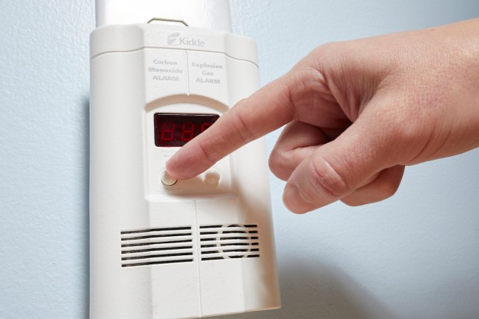 Close up photo of woman pressing the test/reset button on a plugged-in carbon monoxide detector.