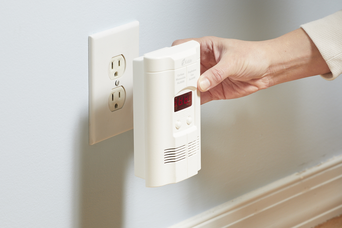 Woman plugs a carbon monoxide detector into a wall outlet.