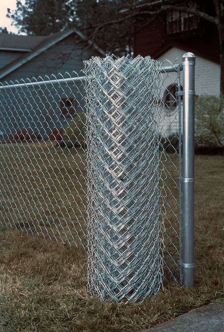 chain link fence installed in home yard with roll of fencing in front