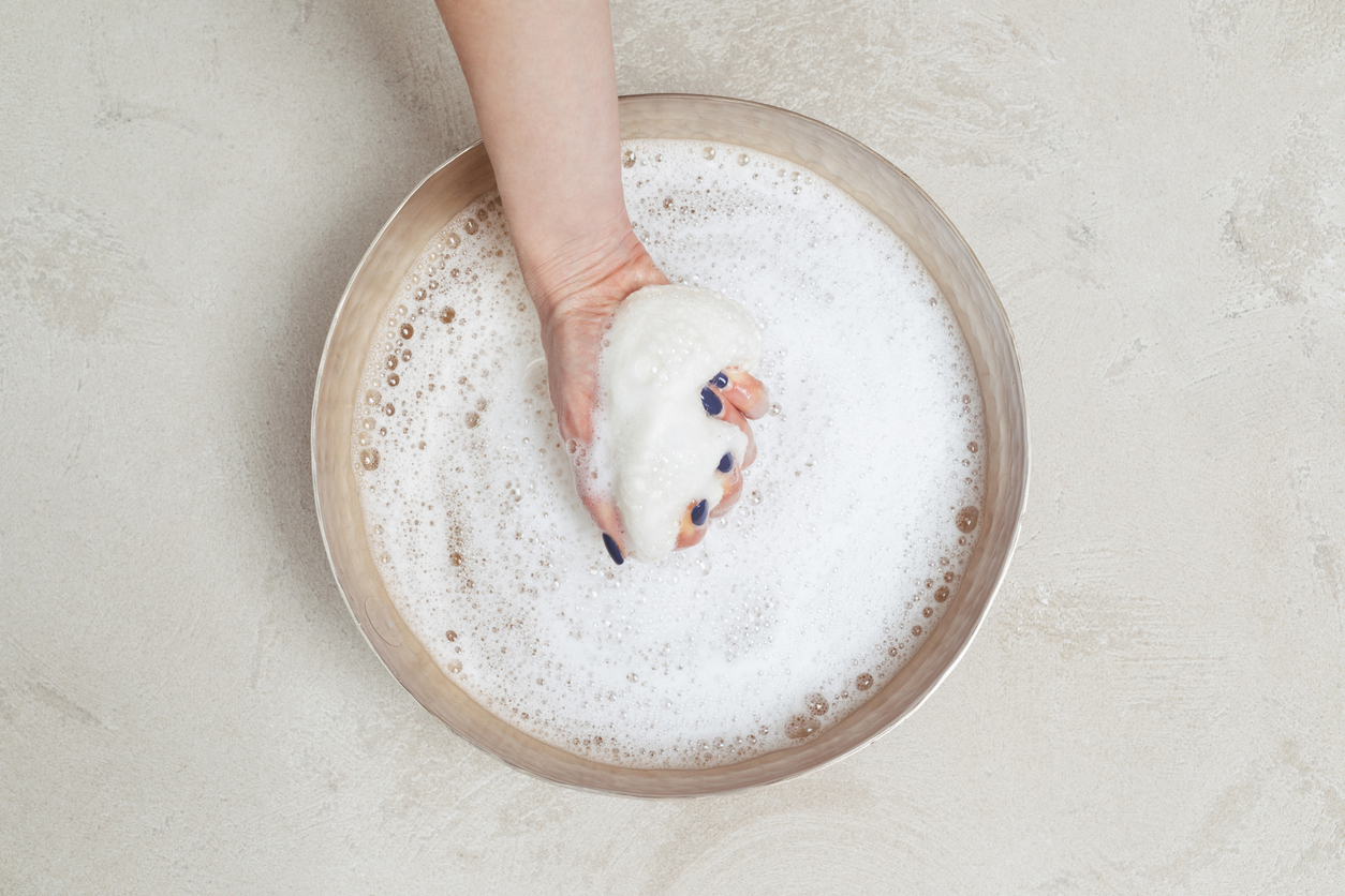 Woman holding soapy cloth over dish of soapy water