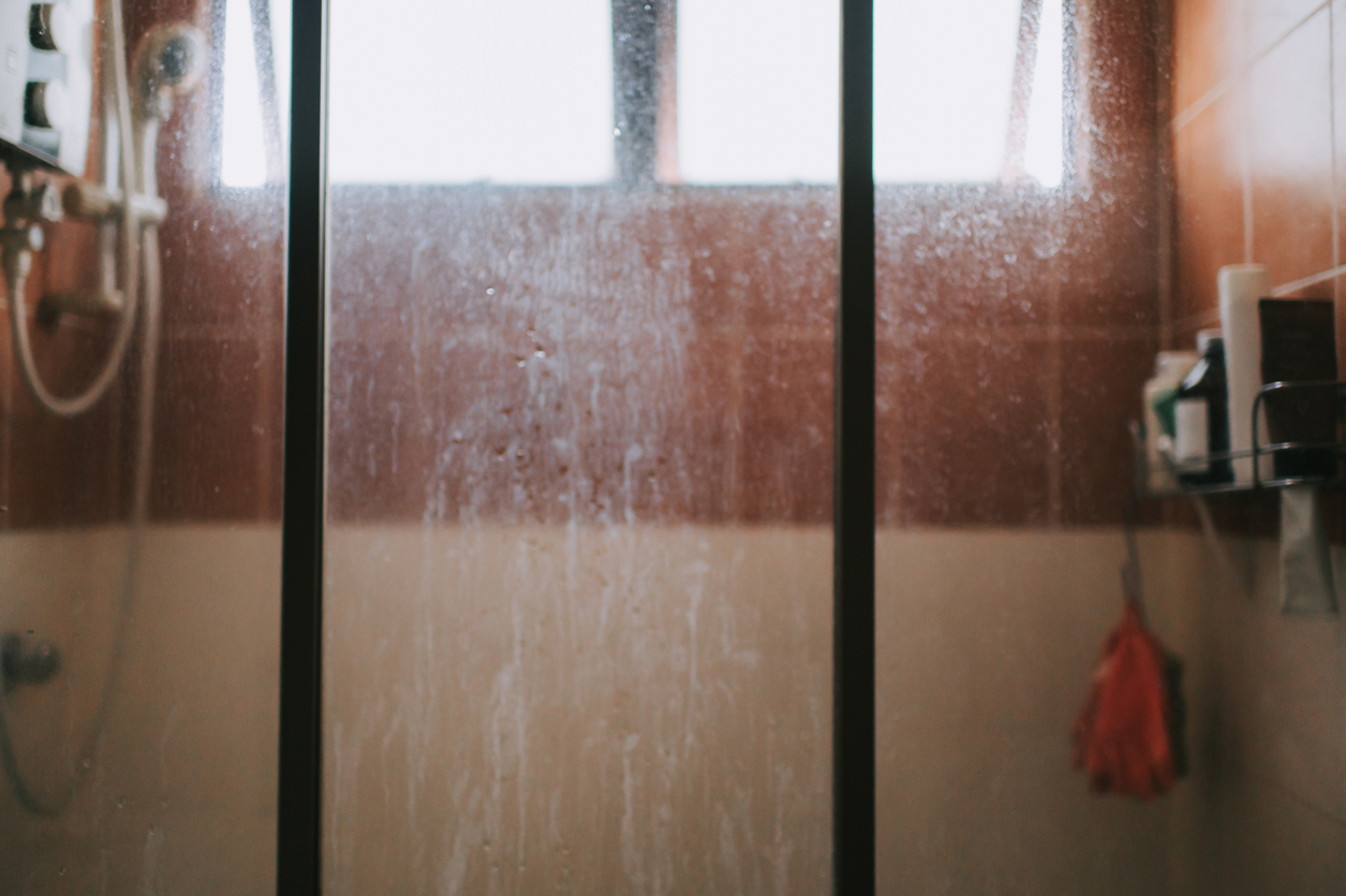 shower door in front of shower with brown tiles with soap scum on glass