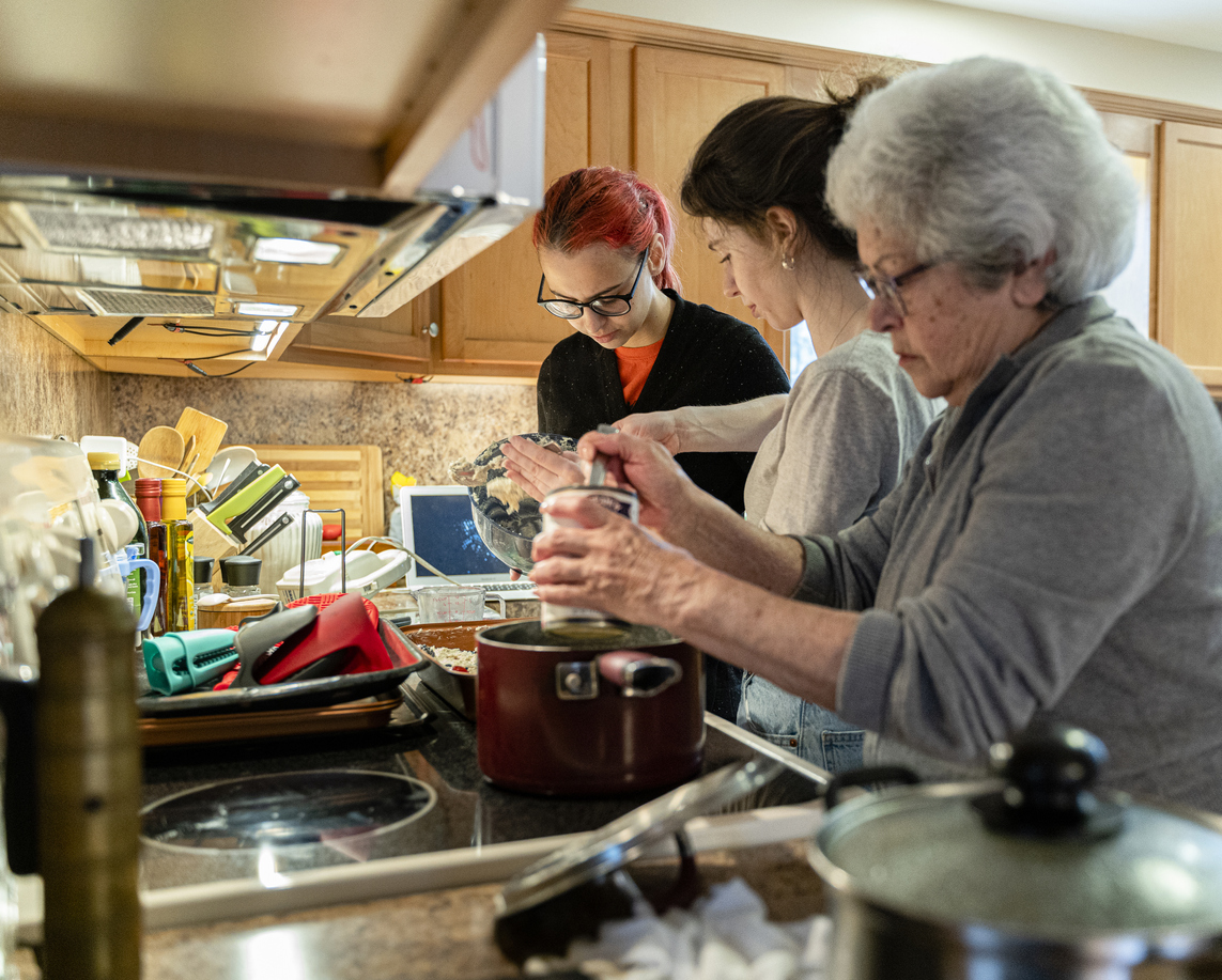 A grandmother is making soup in her home kitchen as her two granddaughters help her make a pie during quarantine.