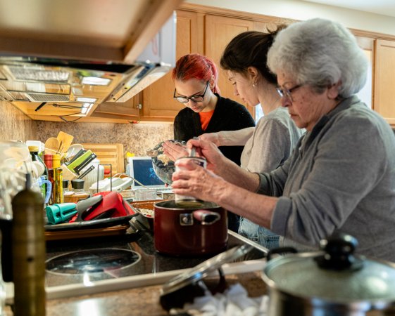 A grandmother is making soup in her home kitchen as her two granddaughters help her make a pie during quarantine.