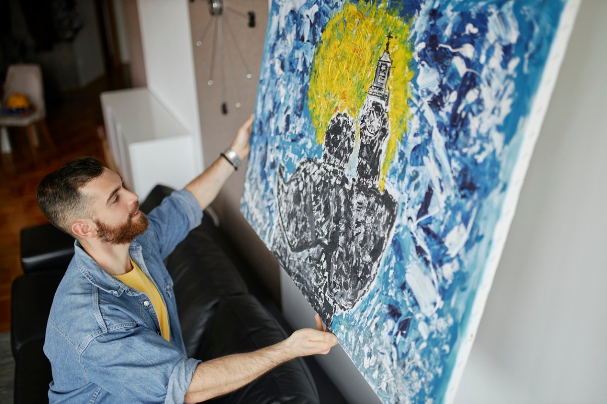 Man with beard hanging a painting on the wall at his living room