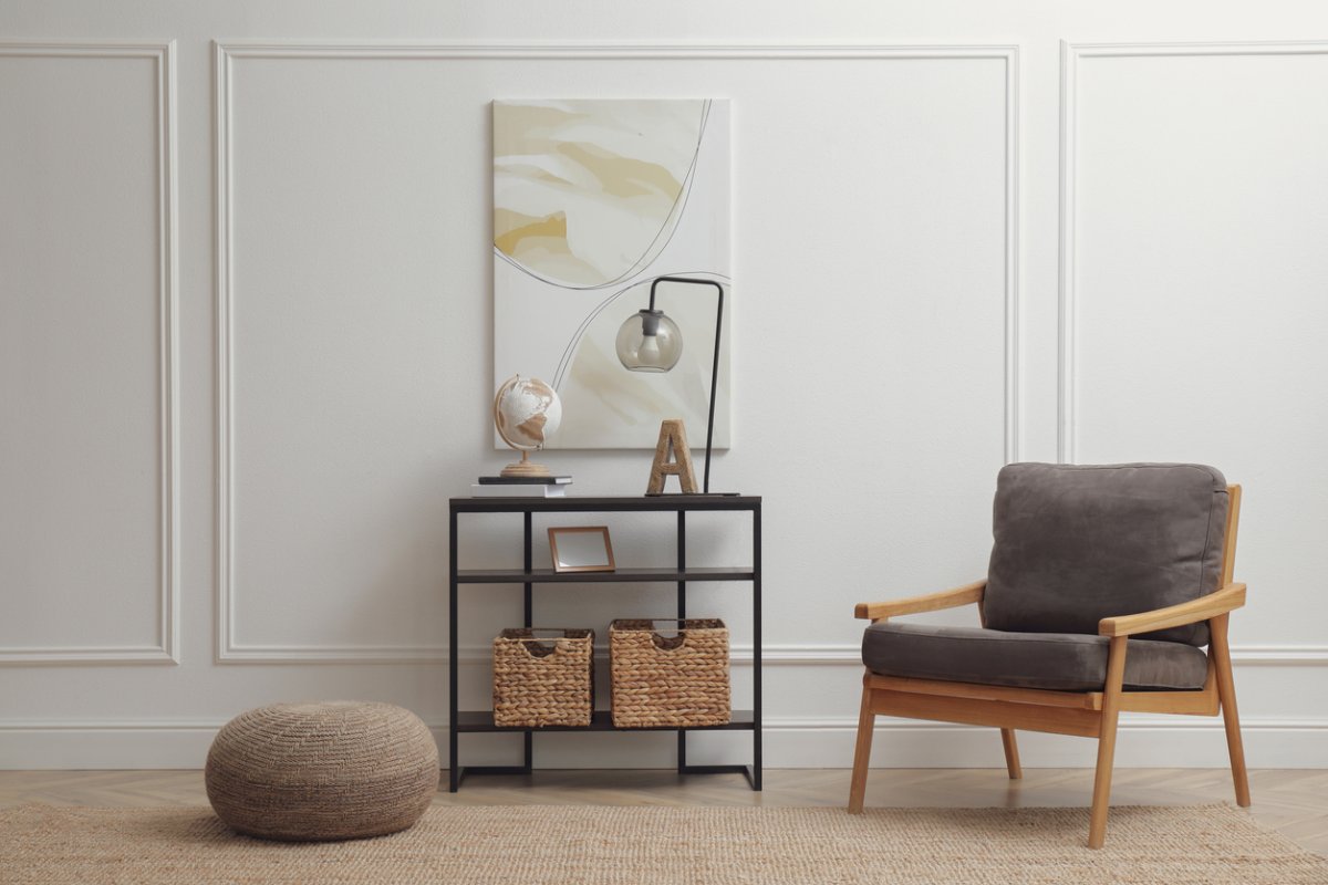 light hallway interior with white wall with trim and stylish console table next to grey chair