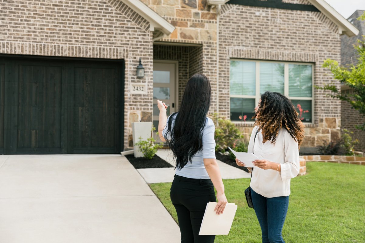 female-inspector-and-homeowner-standing-outside-nice-brick-home-with-landscaped-lawn