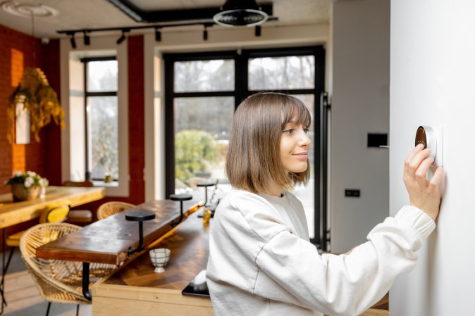 woman adjusting thermostat in home with open plan dining space in background