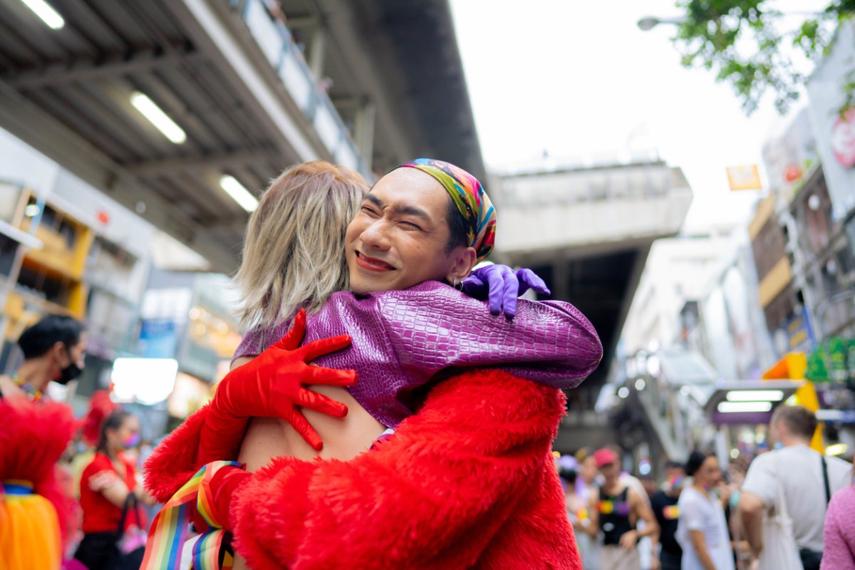 Asian young gay couple embracing and showing their love with rainbow flag at the street.