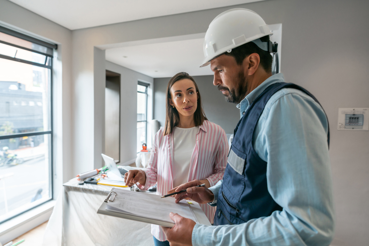 woman speaking to contractor in hard hat holding a clilpboard