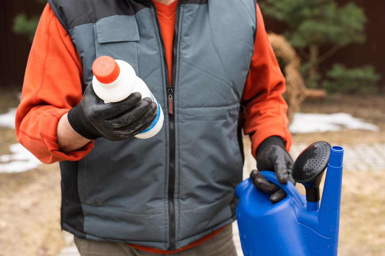 A plastic bottle with chemical weed killer and a watering can in the male hands of farmer