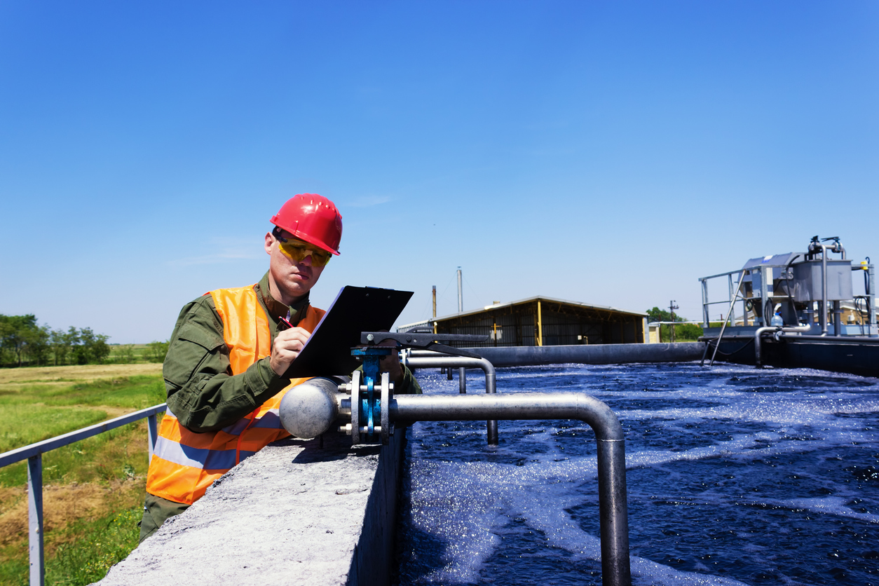 man in hard hat and utility vest holds clip board regulating large water system