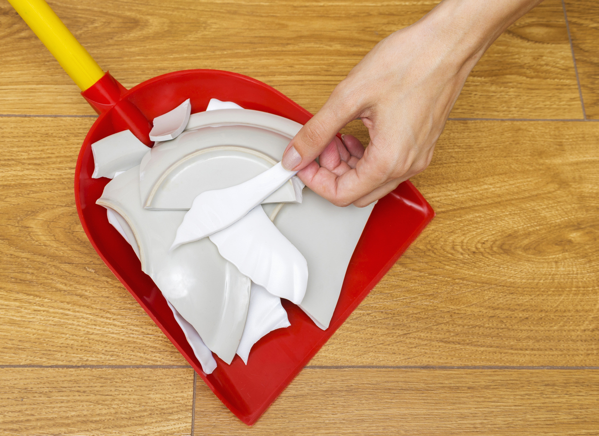 a-hand-places-a-piece-of-broken-ceramics-in-a-red-dustbin-with-other-pieces